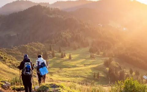 Zwei Wanderer genießen einen **great trail** in Kanada. Die Sonne taucht die bewaldeten Hügel in goldenes Licht.