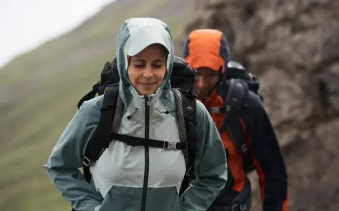 Zwei Wanderer im Regen. Die Frau trägt eine hellblaue Jacke, die perfekt ist, wenn man sich fragt, welche Jacke zum Wandern bei schlechtem Wetter am besten geeignet ist.