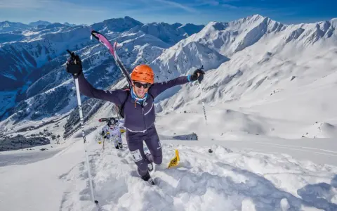 Ein Mann im orangefarbenen Helm jubelt beim Skyrunning in den verschneiten Alpen.