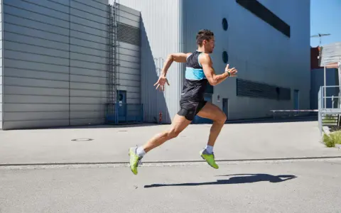 Ein Mann in Sportkleidung läuft mit hoher Kadenz vor einer modernen Industriehalle.
