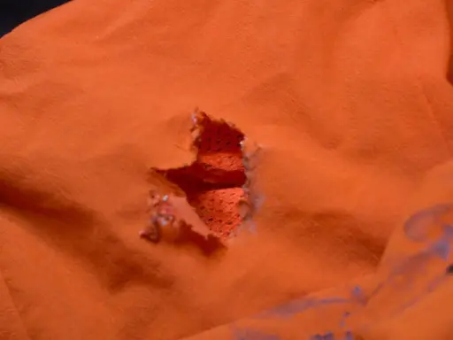 Ein Loch in einer orangefarbenen Polyesterjacke, bereit für einen Flicken.