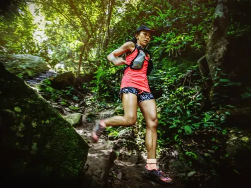 Läuferin bewältigt eine anspruchsvolle ultramarathon distanz auf einem schmalen, steinigen Pfad im dichten Dschungel.
