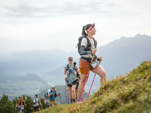 Läuferinnen und Läufer trainieren bergauf gehen in den Alpen. Sie nutzen Stöcke zur Unterstützung.
