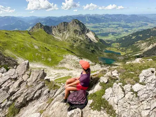 Ein Mädchen mit Rucksack genießt die Aussicht auf die Berge bei Oberstdorf. Ein leichtes Wandern mit toller Belohnung.