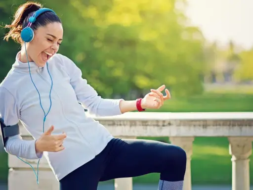 Frau mit Kopfhörern und Handy-Armband spielt Luftgitarre beim Joggen. Die Musik zum Joggen macht sie glücklich.