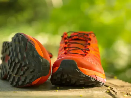 Leuchtend orange Trailrunning-Schuhe mit grobstolliger Sohle, bereit für neue Abenteuer. Perfekt, um bergschuhe neu besohlen zu lassen und wieder loszulegen.