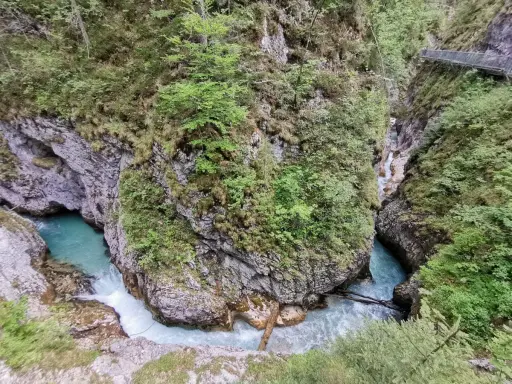Türkisblaues Wasser rauscht durch eine enge Schlucht mit steilen Felswänden, bewachsen mit üppigem Grün. Eine Holzbrücke führt über die Klammen in Bayern.