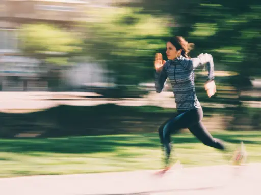 Frau rennt mit Kopfhörern und sportlicher Kleidung, um schneller laufen zu können. Die Bewegung ist durch den leichten Schleier der Geschwindigkeit eingefangen.