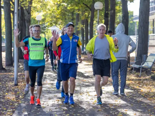 Herren genießen slow jogging im Herbstpark, einige winken fröhlich.