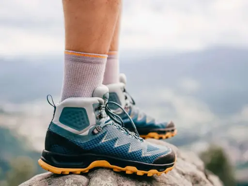 Graue Socken und blaue Wanderschuhe mit gelber Sohle stehen auf einem Felsen. Bereit für das nächste Abenteuer in den Bergen.
