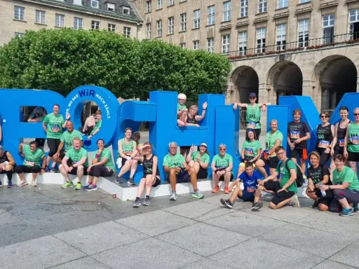 Gruppe feiert Erfolg beim urban run Bochum vor riesiger blauer Schrift.