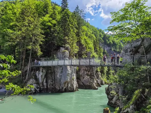 Menschen überqueren eine Hängebrücke während einer entenlochklamm wanderung. Türkises Wasser fließt unter der Brücke hindurch, umgeben von steilen Felswänden und üppigem Grün.