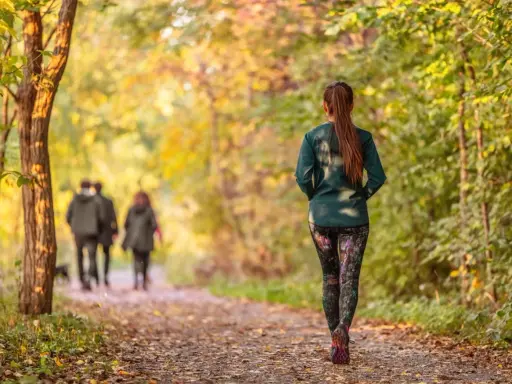 Frau im Herbstwald beim Power Walking, während im Hintergrund ein Paar spazieren geht.
