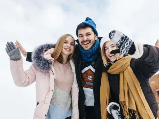 Drei Freunde genießen das Wandern im Winter. Sie tragen warme Kleidung wie Daunenjacken, Mützen und Handschuhe.