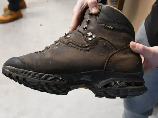 Brauner, abgenutzter Wanderschuh wird gehalten. Die Sohle ist stark abgenutzt, was zeigt, dass die Schuhe besohlen lassen werden müssen, um sie wieder einsatzfähig zu machen.