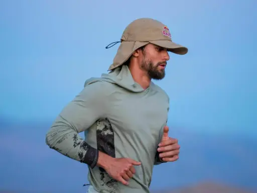 Läufer mit Bart und Sonnenschutz-Cap von Red Bull im Laufschritt, auf dem Weg zum Ultramarathon Weltrekord.