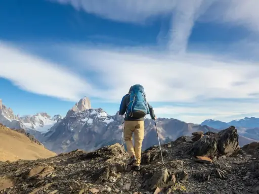 Ein Wanderer mit Rucksack und Stöcken erklimmt einen felsigen Grat. Die majestätische Bergkulisse zeigt die wahre trekking bedeutung: Abenteuer und Freiheit.
