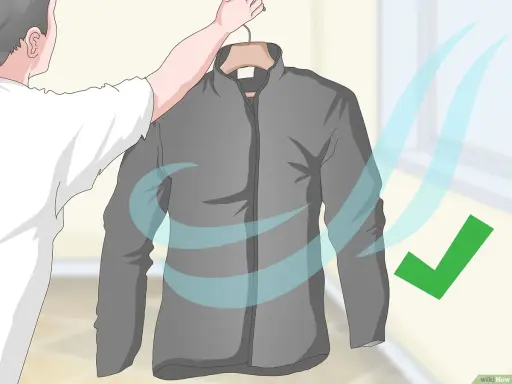 Eine graue Fleecejacke wird zum Trocknen aufgehängt. Blaue Wellen symbolisieren Luftzirkulation, ein grüner Haken zeigt Erfolg an. So wird die Fleecejacke gewaschen und getrocknet.