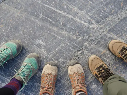 Vier Paar Wanderschuhe auf grauem Steinboden. Sie zeigen, wie sollten Wanderschuhe sitzen: bequem, aber fest.