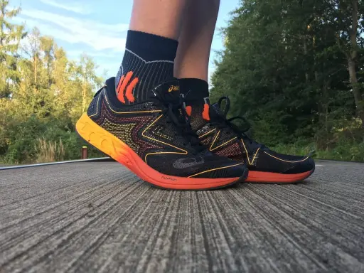 Asics Gel NoosaFast Laufschuhe in Schwarz mit orangen Akzenten, bereit für den nächsten Lauf im Grünen.