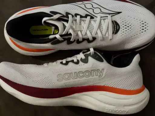Zwei weiße Laufschuhe, die Saucony Ride 19, mit roten und orangen Akzenten. Perfekt für neutrale Läufer.