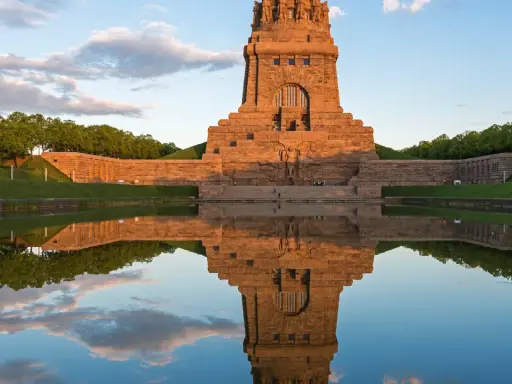Das Völkerschlachtdenkmal in Leipzig spiegelt sich im Wasser. Ein Läufer genießt die Abendstimmung.