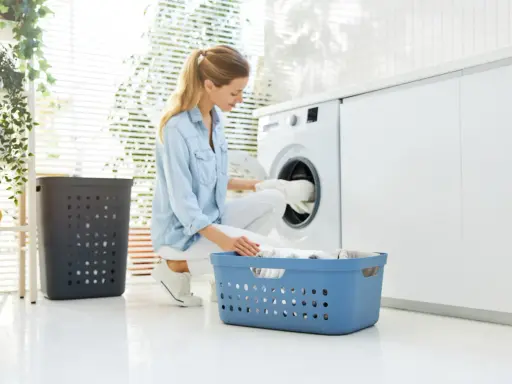Frau lädt Wäsche in die Waschmaschine. So kann man eine Daunenjacke waschen ohne Trockner.