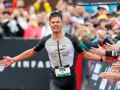 Triathlet Rico feiert seinen Zieleinlauf beim Ironman Luxembourg. Jubelnde Zuschauer reichen ihm die Hände.
