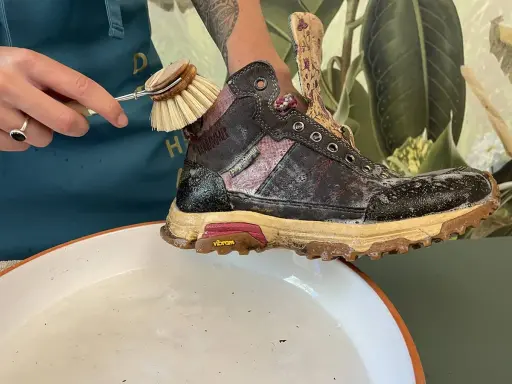 Schuhbürste reinigt schmutzige Wanderschuhe in Seifenwasser. So pflegen Sie Ihre Wanderschuhe richtig.