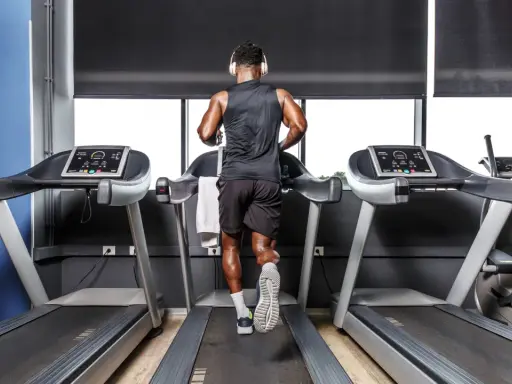 Mann mit Kopfhörern absolviert ein intensives Laufband Training im Fitnessstudio.