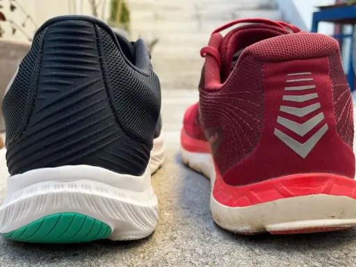 Zwei Laufschuhe, ein schwarzer und ein roter, stehen nebeneinander. Der rote Schuh trägt das Logo "altra rivera".