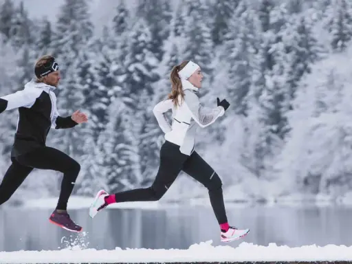 Zwei Läufer in warmer Winterkleidung genießen einen Lauf im Schnee.