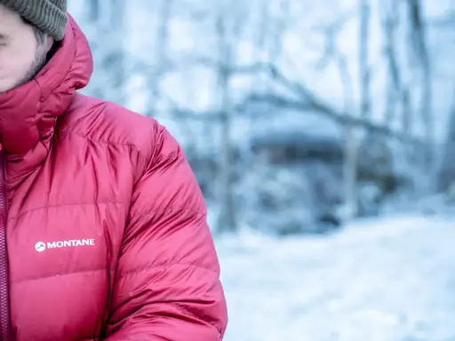 Mann in roter Montane-Jacke mit Kapuze im Schnee. Gute thermore ecodown erfahrungen im Winter.