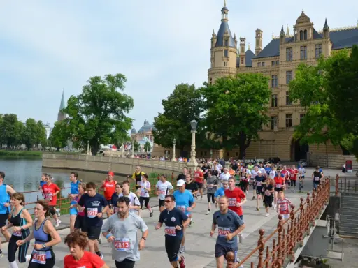 Teilnehmer des 5 Seen Lauf Schwerin überqueren eine Brücke vor dem Schloss.