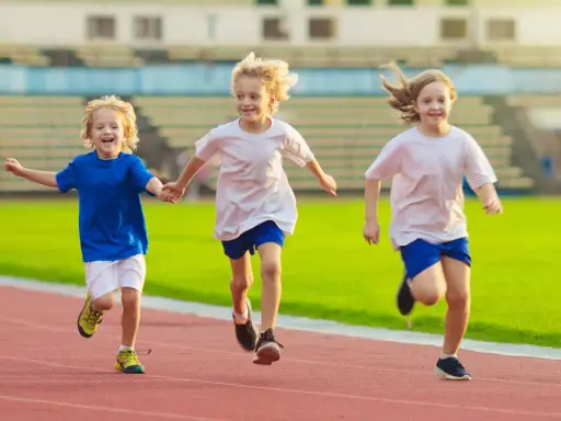 Drei lachende Kinder beim Lauftraining auf einer roten Laufbahn. Sie rennen nebeneinander, die Arme ausgestreckt.
