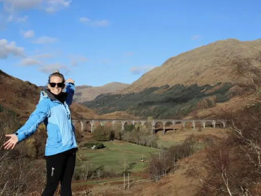 Glückliche Frau genießt das Wandern in Schottland vor einer beeindruckenden Brücke in den Highlands.