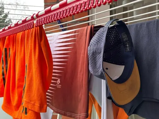 Wäscheleine mit Kleidung, darunter ein orangefarbenes Shirt, ein braunes Shirt und eine Kappe, die zum cap reinigen aufgehängt wurde.