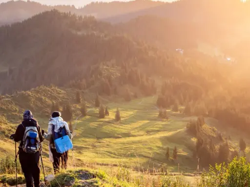 Zwei Wanderer genießen einen **great trail** in Kanada. Die Sonne taucht die bewaldeten Hügel in goldenes Licht.