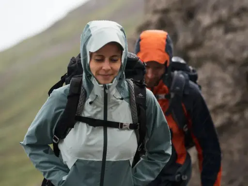Zwei Wanderer im Regen. Die Frau trägt eine hellblaue Jacke, die perfekt ist, wenn man sich fragt, welche Jacke zum Wandern bei schlechtem Wetter am besten geeignet ist.