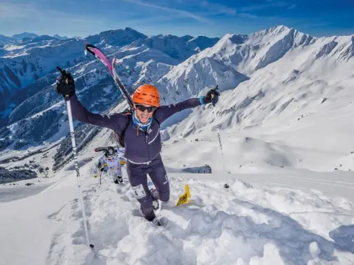 Ein Mann im orangefarbenen Helm jubelt beim Skyrunning in den verschneiten Alpen.