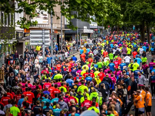 Große Menschenmenge beim Firmenlauf Essen, viele Läufer in bunten Trikots auf einer Straße, umgeben von Bäumen und Gebäuden.