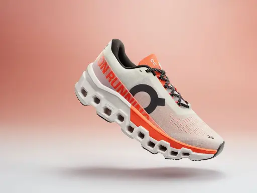 Ein weißer Laufschuh mit orangefarbenen Akzenten, der Cloudmonster 2 Herren, schwebt vor einem sanften Farbverlauf.