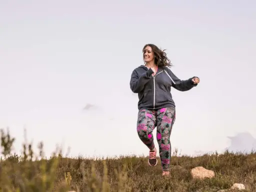 Frau joggt mit Gewichten in bunter Hose durch die Natur.