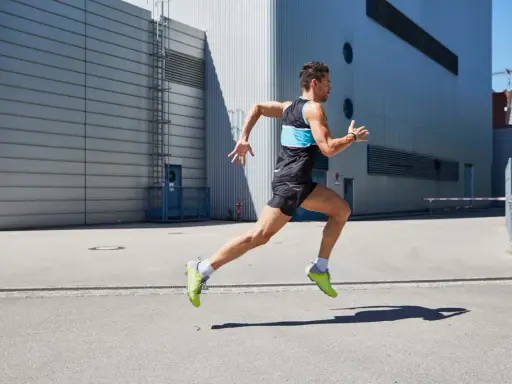 Ein Mann in Sportkleidung läuft mit hoher Kadenz vor einer modernen Industriehalle.