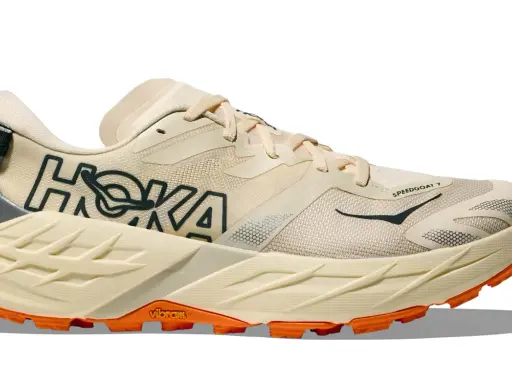 Beiger Hoka Speedgoat 7 Trailrunningschuh mit orangefarbener Vibram-Sohle und dunklem Hoka-Logo.