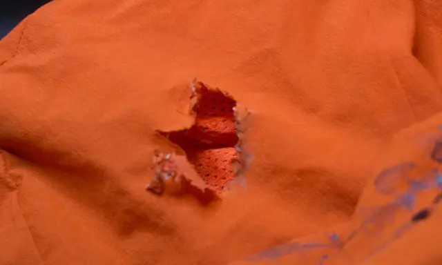 Ein Loch in einer orangefarbenen Polyesterjacke, bereit für einen Flicken.