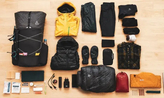 Rucksack, Wanderstöcke, gelbe Regenjacke, Daunenjacke, Handschuhe, Schlafsack, Zelt und Kleidung für **ultralight trekking**.