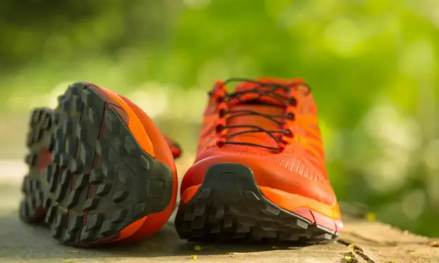Leuchtend orange Trailrunning-Schuhe mit grobstolliger Sohle, bereit für neue Abenteuer. Perfekt, um bergschuhe neu besohlen zu lassen und wieder loszulegen.