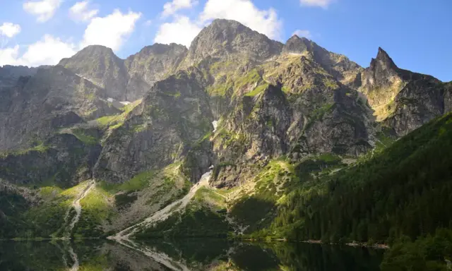 Majestätische Berge im Tatra Gebirge laden zum Wandern ein. Ein ruhiger See spiegelt die felsigen Hänge und den blauen Himmel wider.