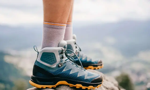 Graue Socken und blaue Wanderschuhe mit gelber Sohle stehen auf einem Felsen. Bereit für das nächste Abenteuer in den Bergen.